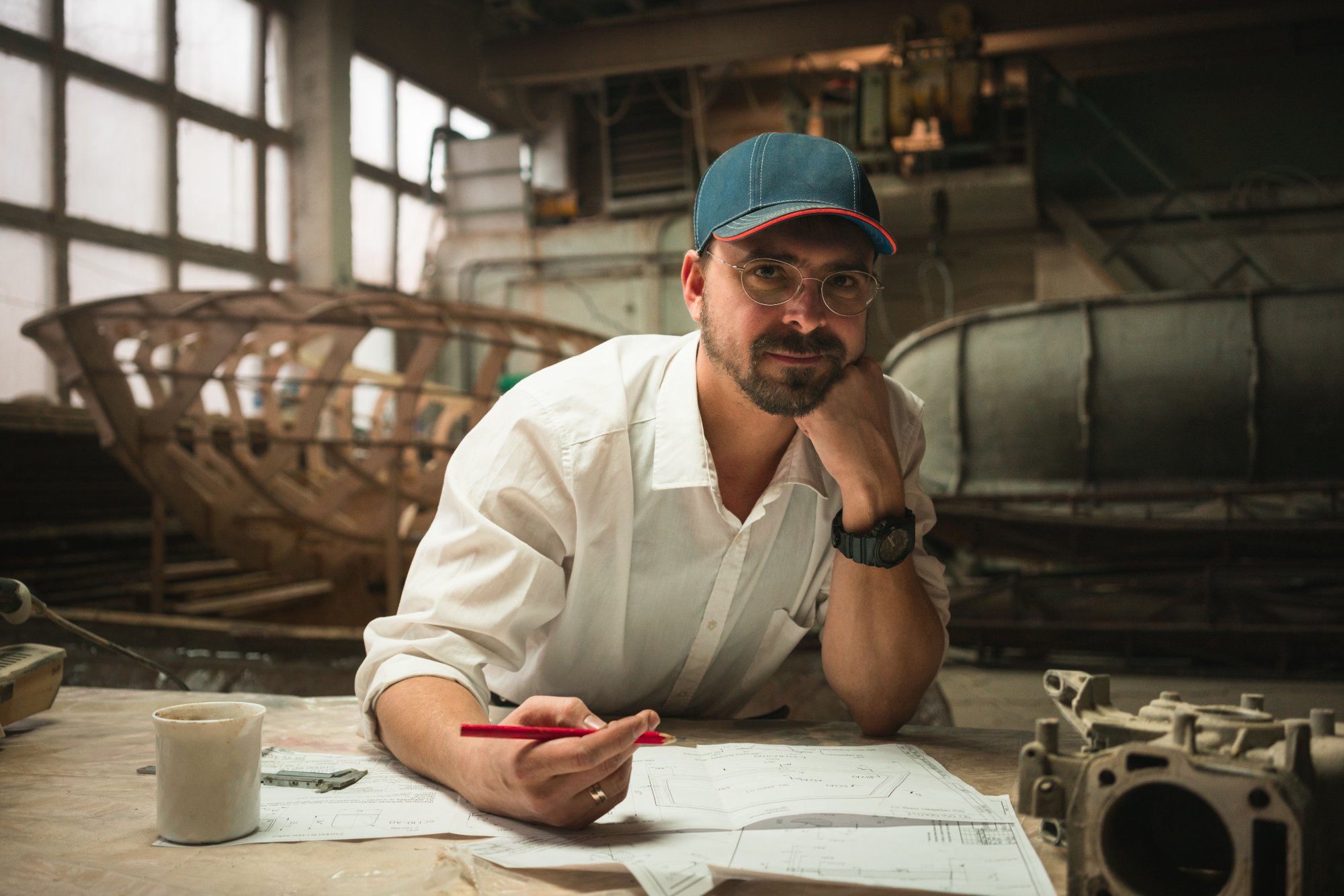 Engineer reviewing technical drawings in a boatyard workshop with hull frames in the background