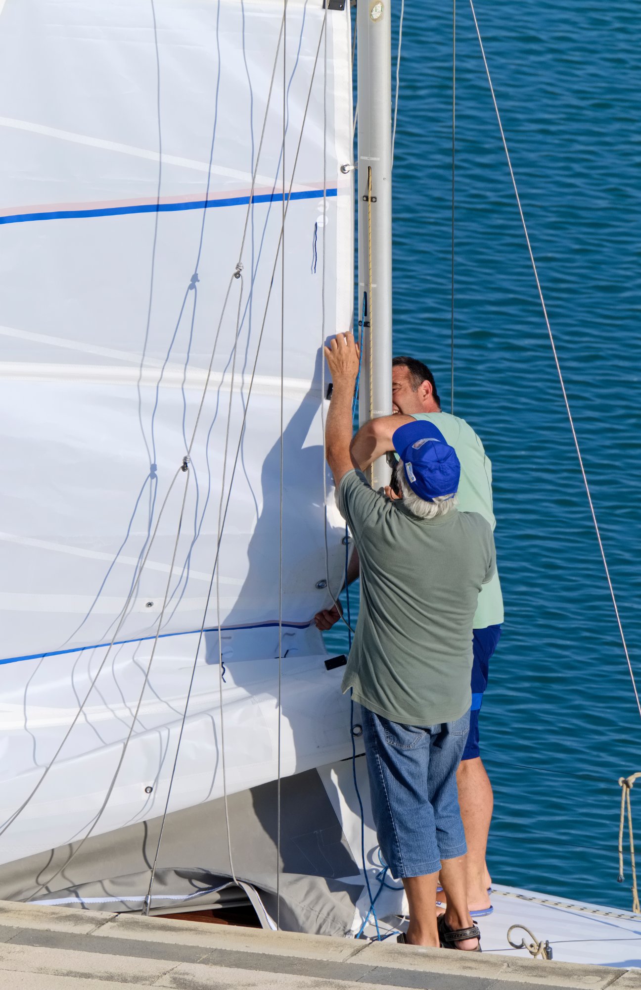 Two sailors inspecting a mainsail at the mast on a docked racing yacht