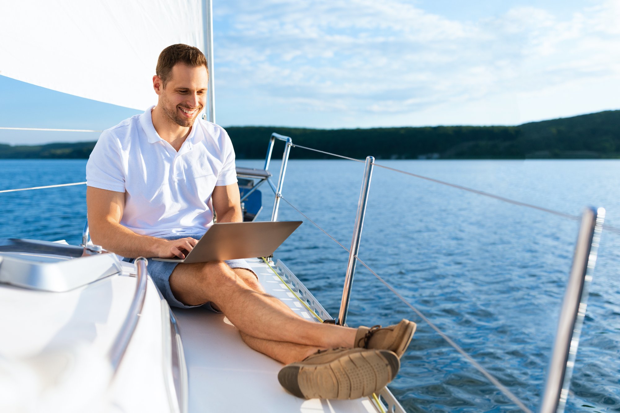 Sailor reviewing data on laptop aboard a sailboat at anchor