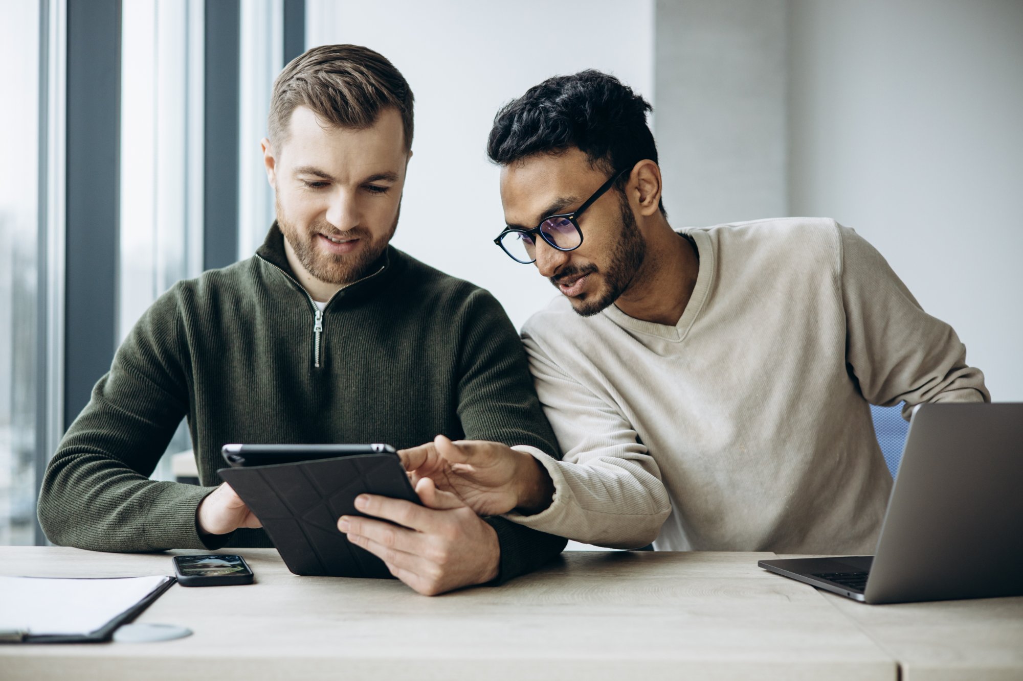 Two colleagues reviewing performance data together on a tablet in a modern workspace