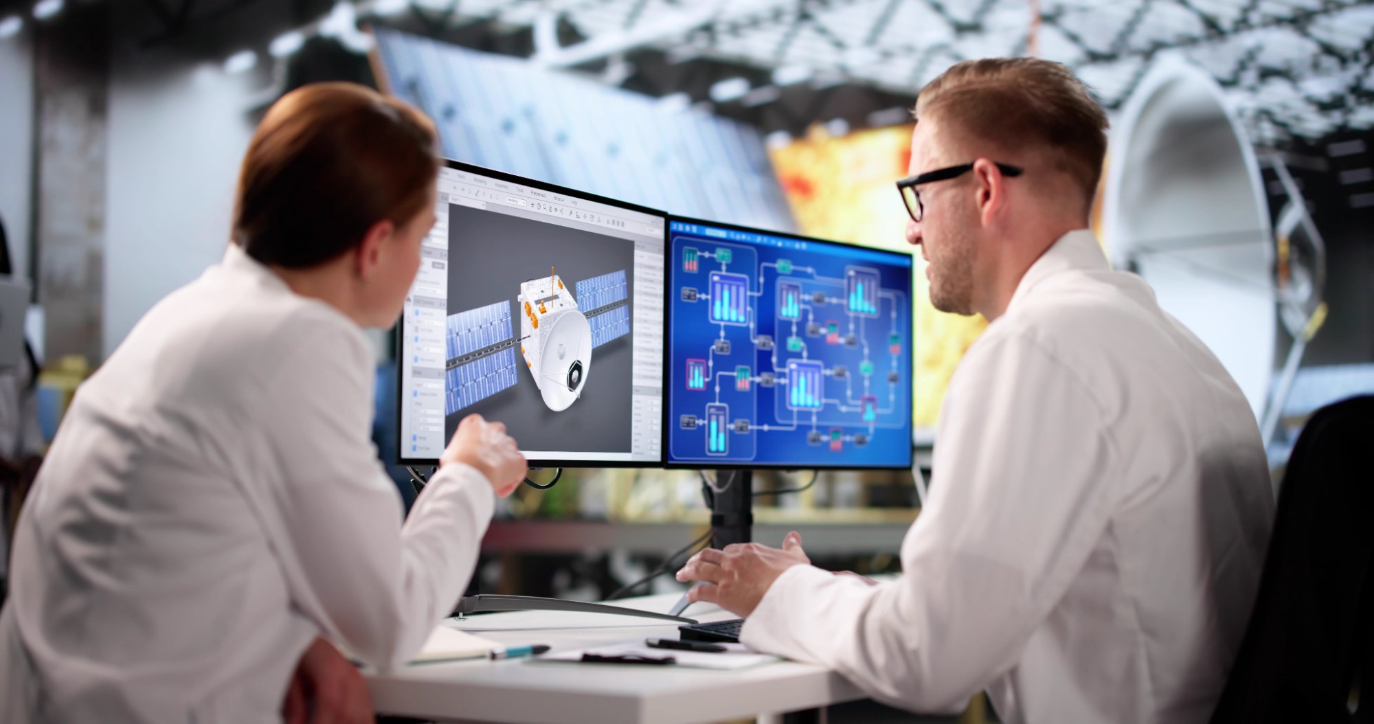 Two engineers collaborating at dual monitors reviewing 3D model and system diagrams